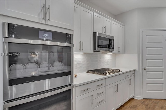 kitchen featuring white cabinetry, backsplash, stainless steel appliances, and light hardwood / wood-style floors