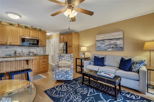 living room featuring ornamental molding, ceiling fan, a textured ceiling, and light hardwood / wood-style flooring