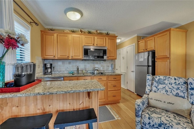 kitchen with crown molding, light hardwood / wood-style flooring, a breakfast bar area, and appliances with stainless steel finishes