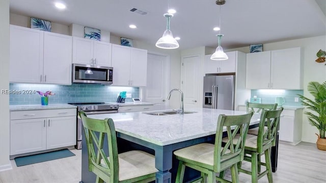 kitchen featuring sink, white cabinetry, pendant lighting, stainless steel appliances, and a kitchen island with sink