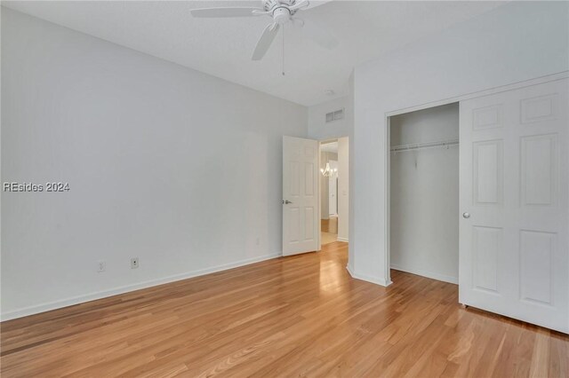 unfurnished bedroom featuring ceiling fan with notable chandelier, a closet, and light wood-type flooring