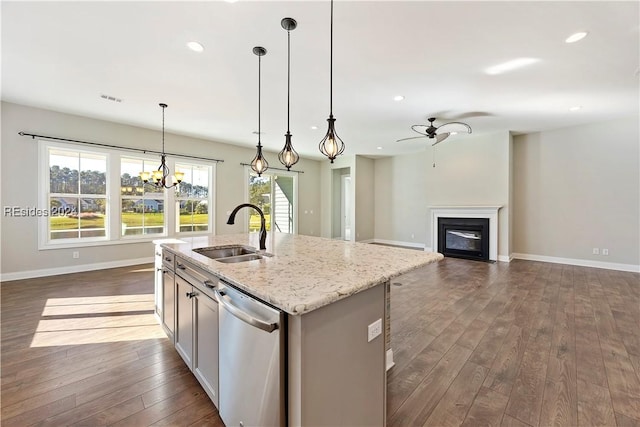 kitchen featuring sink, a kitchen island with sink, light stone counters, decorative light fixtures, and stainless steel dishwasher