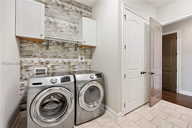 washroom featuring light tile patterned floors, wooden walls, washing machine and dryer, and cabinets