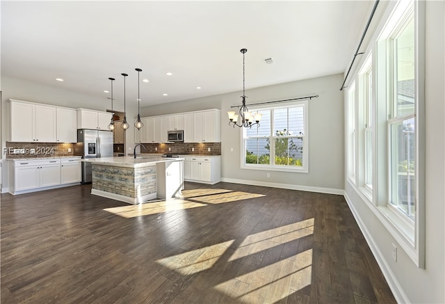 kitchen with a center island with sink, appliances with stainless steel finishes, dark hardwood / wood-style flooring, pendant lighting, and white cabinets