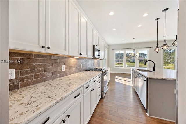 kitchen featuring pendant lighting, sink, white cabinets, stainless steel appliances, and light stone countertops