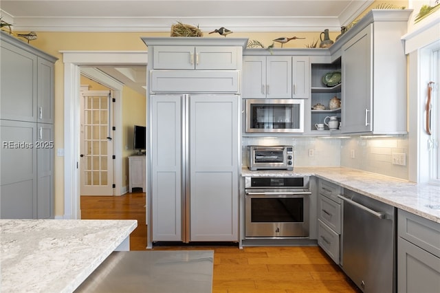 kitchen featuring tasteful backsplash, built in appliances, light wood-type flooring, gray cabinets, and light stone countertops