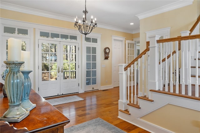 entrance foyer featuring an inviting chandelier, crown molding, wood-type flooring, and french doors