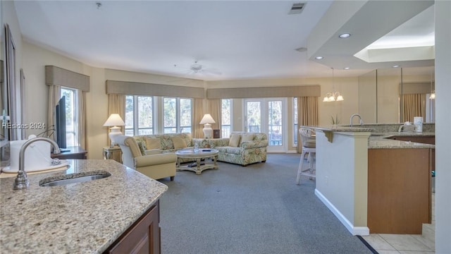 carpeted living room with sink and ceiling fan with notable chandelier