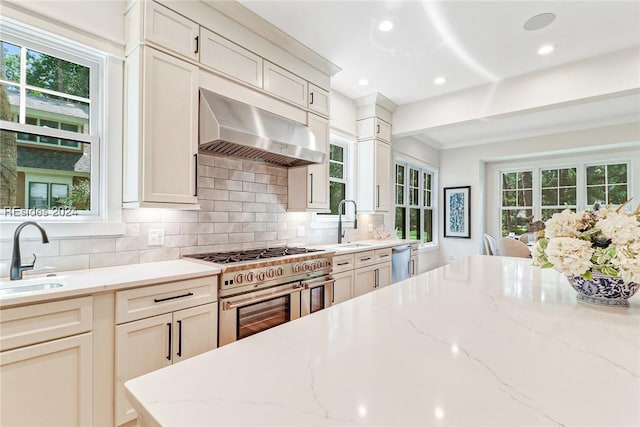 kitchen featuring appliances with stainless steel finishes, exhaust hood, backsplash, and light stone counters