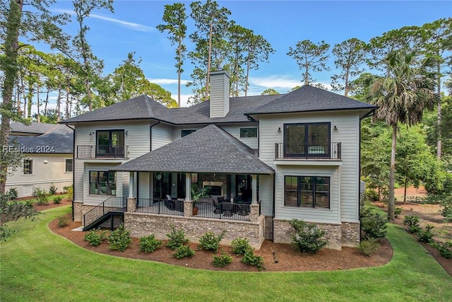 back of property with a balcony, a patio area, and a lawn