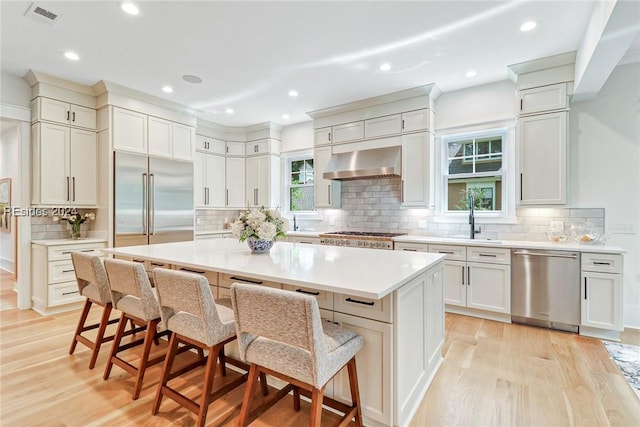 kitchen featuring appliances with stainless steel finishes, a breakfast bar, a center island, light wood-type flooring, and wall chimney exhaust hood