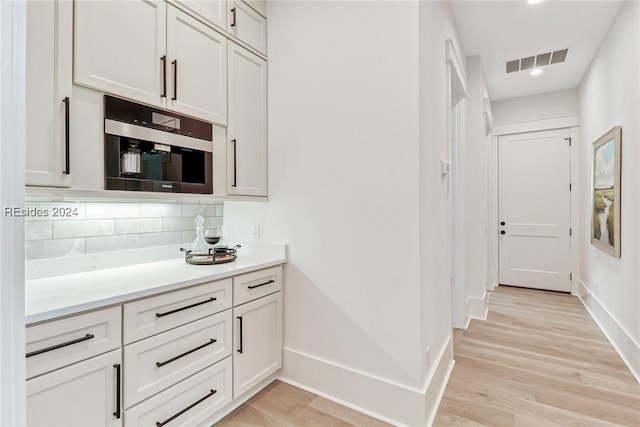 kitchen with white cabinets, backsplash, and light wood-type flooring