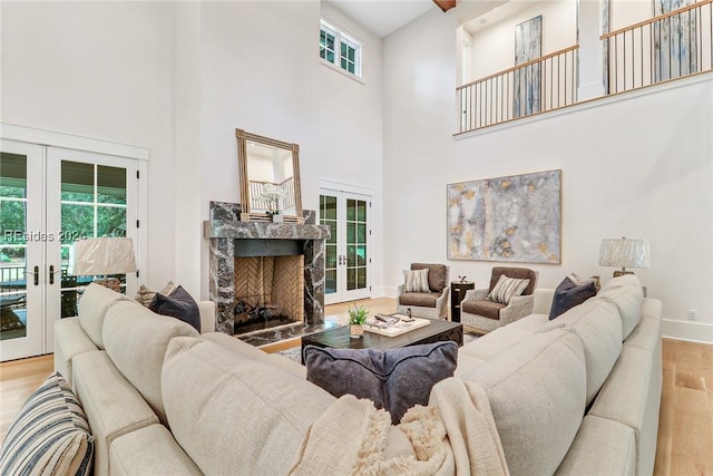 living room featuring a premium fireplace, light hardwood / wood-style floors, french doors, and a high ceiling