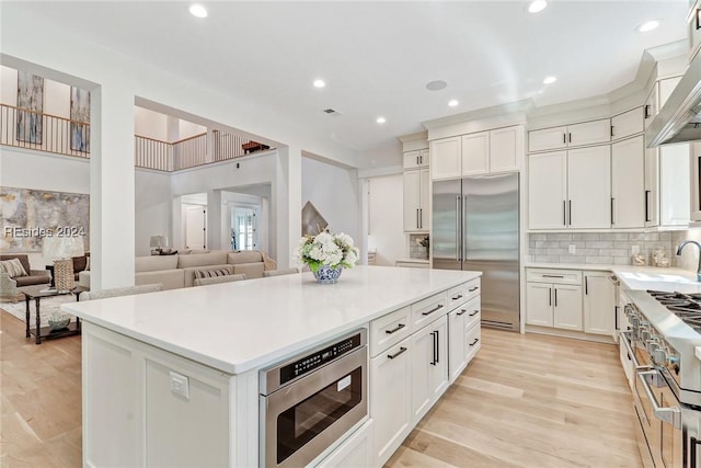 kitchen with sink, white cabinetry, built in appliances, a kitchen island, and decorative backsplash