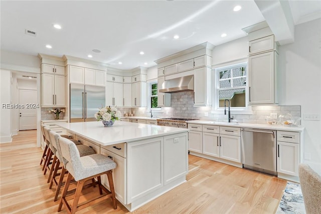 kitchen featuring a breakfast bar, sink, a center island, appliances with stainless steel finishes, and exhaust hood