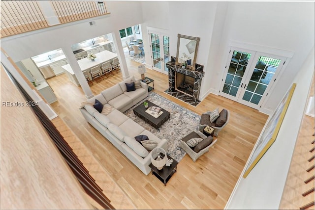 living room with a stone fireplace, a towering ceiling, hardwood / wood-style floors, and french doors