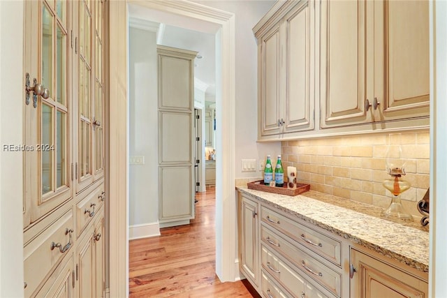 bar with tasteful backsplash, light hardwood / wood-style flooring, light stone counters, and cream cabinetry