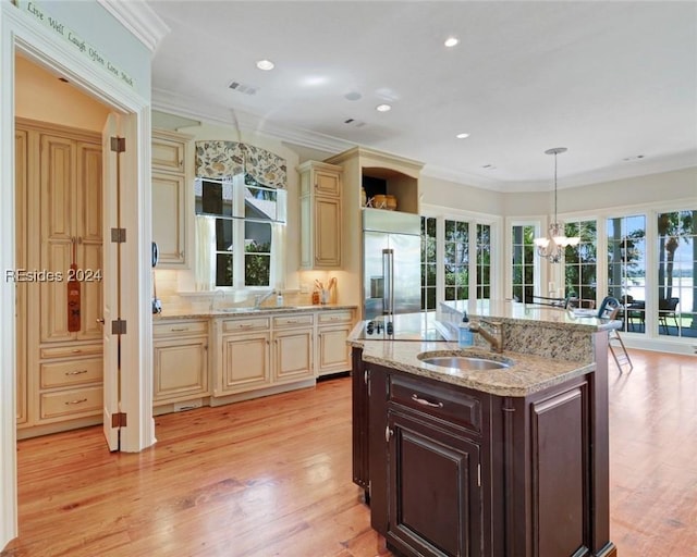 kitchen featuring built in fridge, decorative light fixtures, sink, cream cabinets, and dark brown cabinets