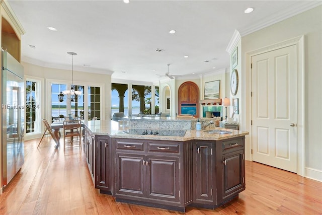 kitchen with sink, a kitchen island with sink, hanging light fixtures, dark brown cabinetry, and ornamental molding