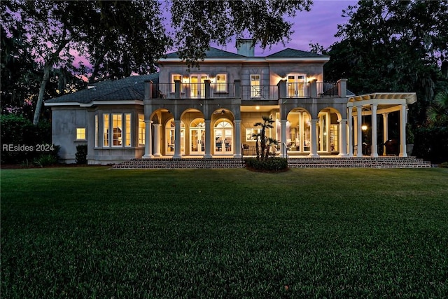 back house at dusk with a balcony and a lawn