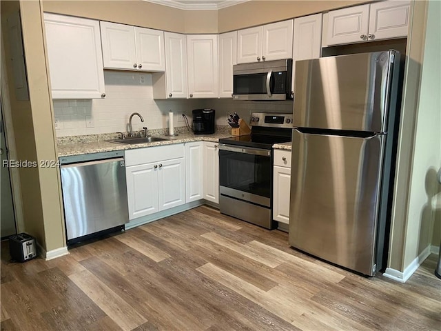 kitchen featuring sink, hardwood / wood-style flooring, appliances with stainless steel finishes, white cabinetry, and light stone countertops