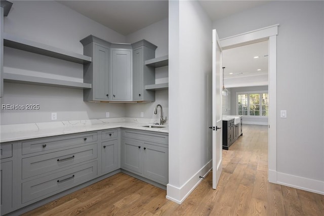 kitchen featuring sink, gray cabinetry, light stone counters, and light hardwood / wood-style floors