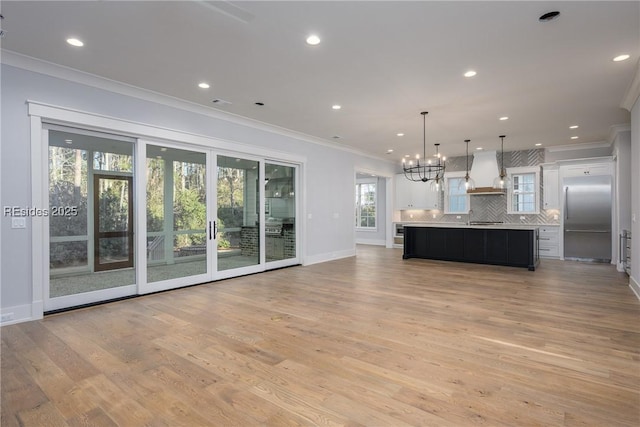 kitchen with white cabinetry, hanging light fixtures, stainless steel built in fridge, custom range hood, and a spacious island