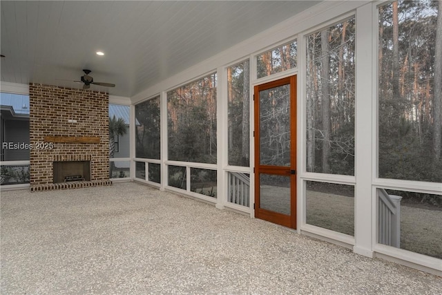 unfurnished sunroom with ceiling fan, a healthy amount of sunlight, and a brick fireplace