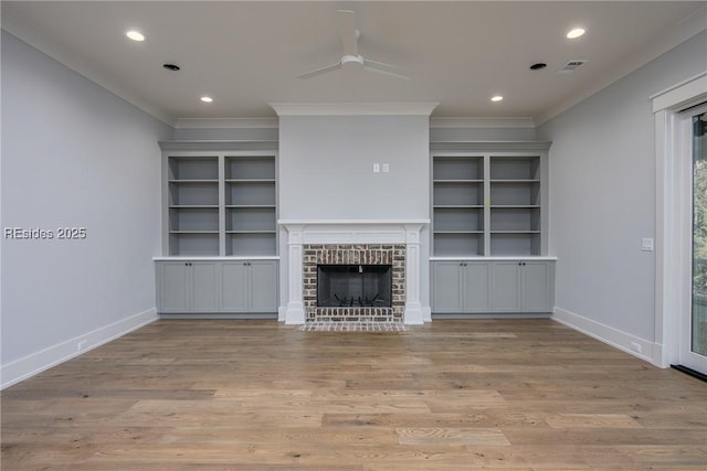 unfurnished living room with ceiling fan, ornamental molding, a brick fireplace, and light wood-type flooring