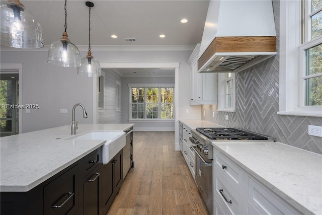 kitchen featuring an island with sink, custom range hood, sink, and white cabinets