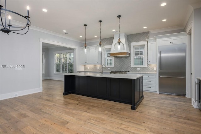 kitchen with white cabinetry, stainless steel built in fridge, and a center island with sink