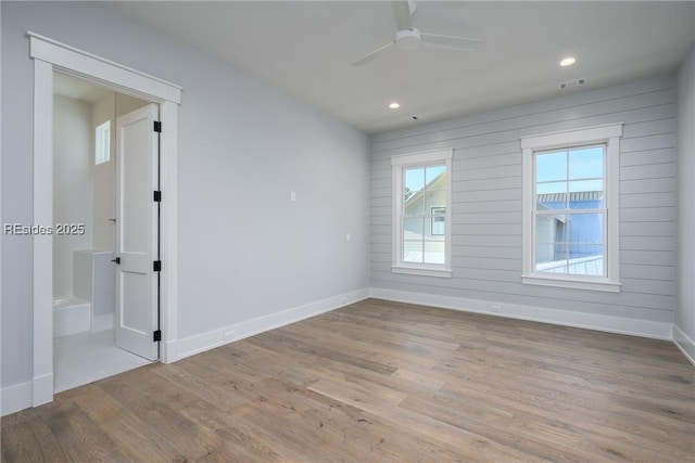 spare room with ceiling fan, wooden walls, and light hardwood / wood-style flooring