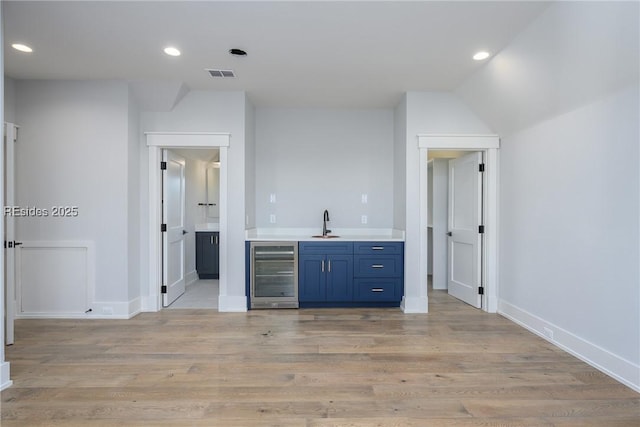 bar with sink, blue cabinetry, wine cooler, light hardwood / wood-style floors, and vaulted ceiling