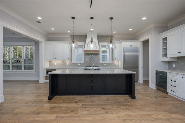 kitchen featuring wine cooler, built in refrigerator, hanging light fixtures, a kitchen island with sink, and white cabinets