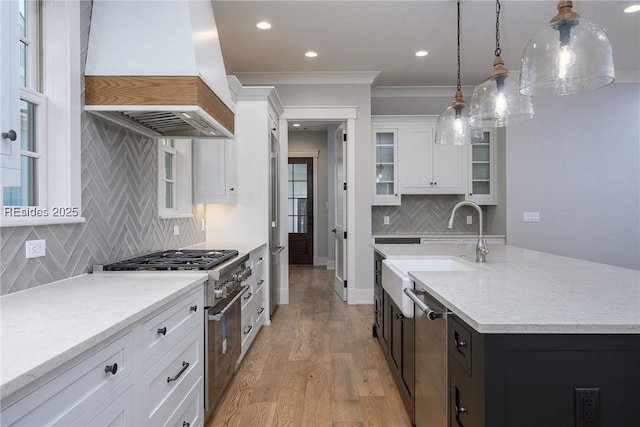 kitchen featuring premium range hood, tasteful backsplash, decorative light fixtures, an island with sink, and white cabinets