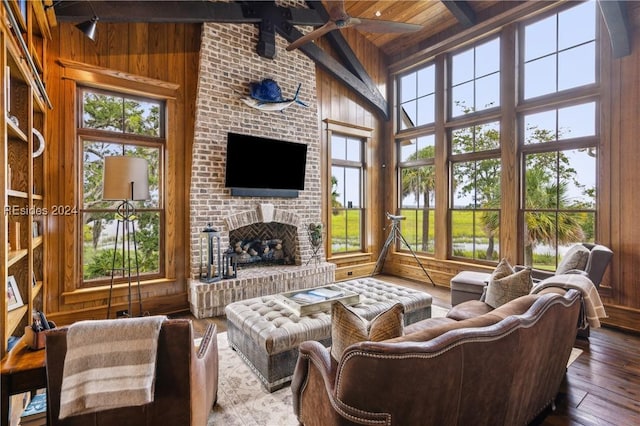 living room with beam ceiling, plenty of natural light, a fireplace, wood-type flooring, and wood walls