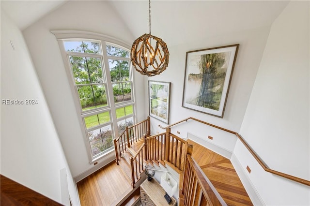 staircase featuring wood-type flooring, vaulted ceiling, and a notable chandelier