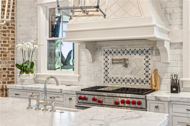 kitchen featuring sink, tasteful backsplash, white cabinetry, high end range, and light stone countertops