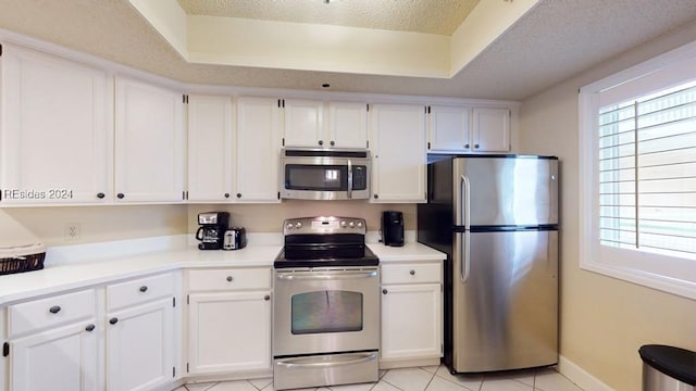 kitchen with appliances with stainless steel finishes, white cabinetry, a textured ceiling, light tile patterned flooring, and a raised ceiling