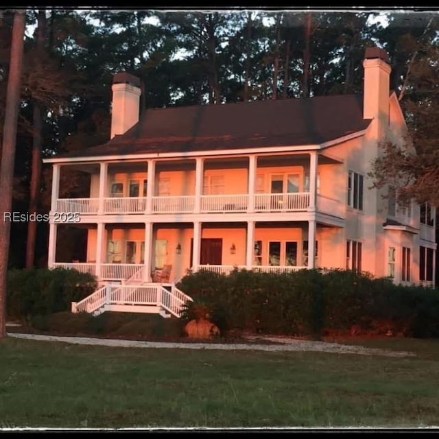 rear view of house featuring a balcony, a porch, and a lawn