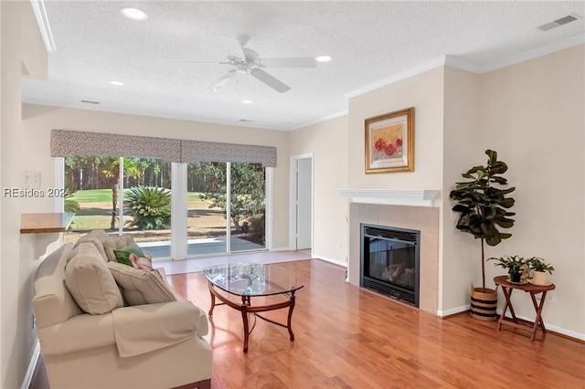 living room featuring wood-type flooring, a textured ceiling, ornamental molding, ceiling fan, and a fireplace