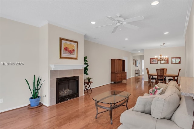 living room featuring hardwood / wood-style flooring, ceiling fan with notable chandelier, a tile fireplace, and a textured ceiling