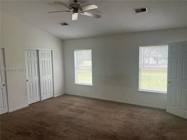 spare room with lofted ceiling, a healthy amount of sunlight, a textured ceiling, and dark colored carpet