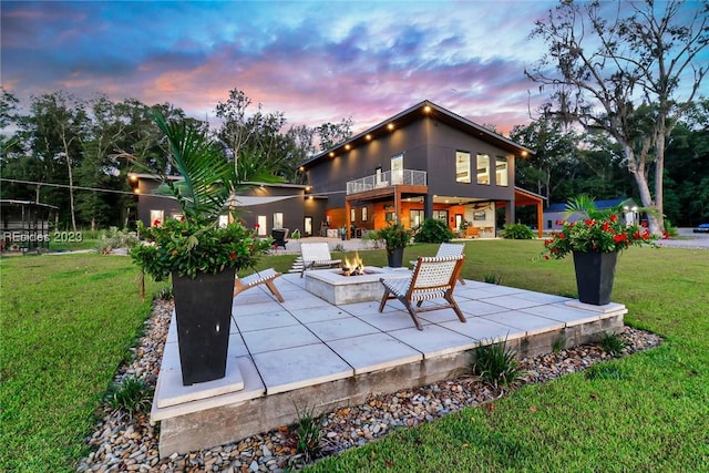 patio terrace at dusk with a balcony, a yard, and a fire pit