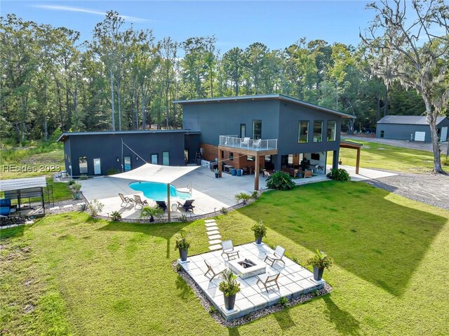 rear view of house with a balcony, an outdoor fire pit, a patio area, and a lawn