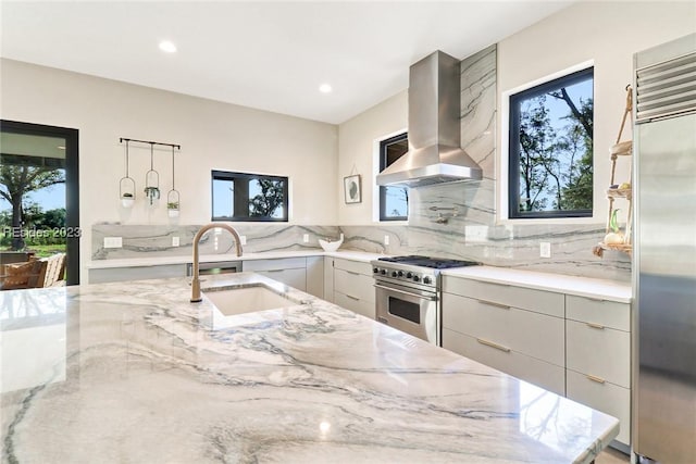 kitchen with high end appliances, sink, light stone counters, and range hood