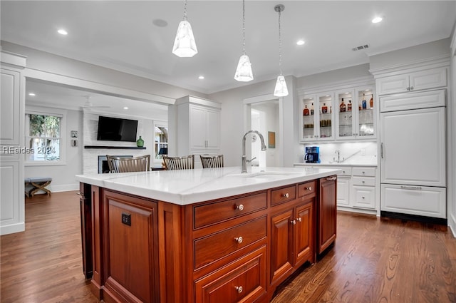 kitchen featuring sink, white cabinets, hanging light fixtures, a kitchen island with sink, and dark wood-type flooring