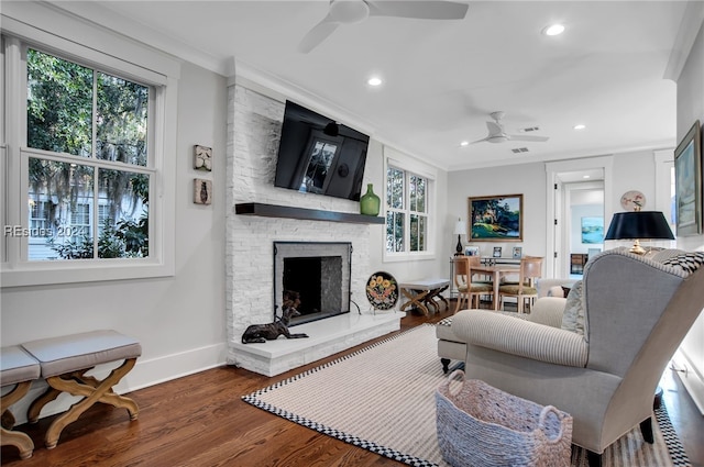 living room with a healthy amount of sunlight, a fireplace, ornamental molding, and wood-type flooring