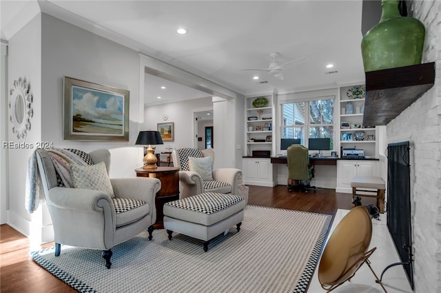 living room featuring a stone fireplace, ceiling fan, hardwood / wood-style floors, built in desk, and built in shelves