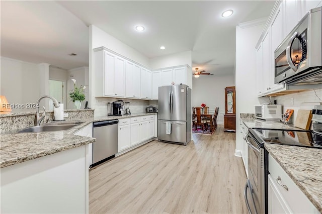 kitchen featuring sink, white cabinetry, stainless steel appliances, light stone countertops, and light wood-type flooring